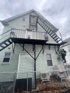 A man is standing on a ladder on the side of a house with stairs.