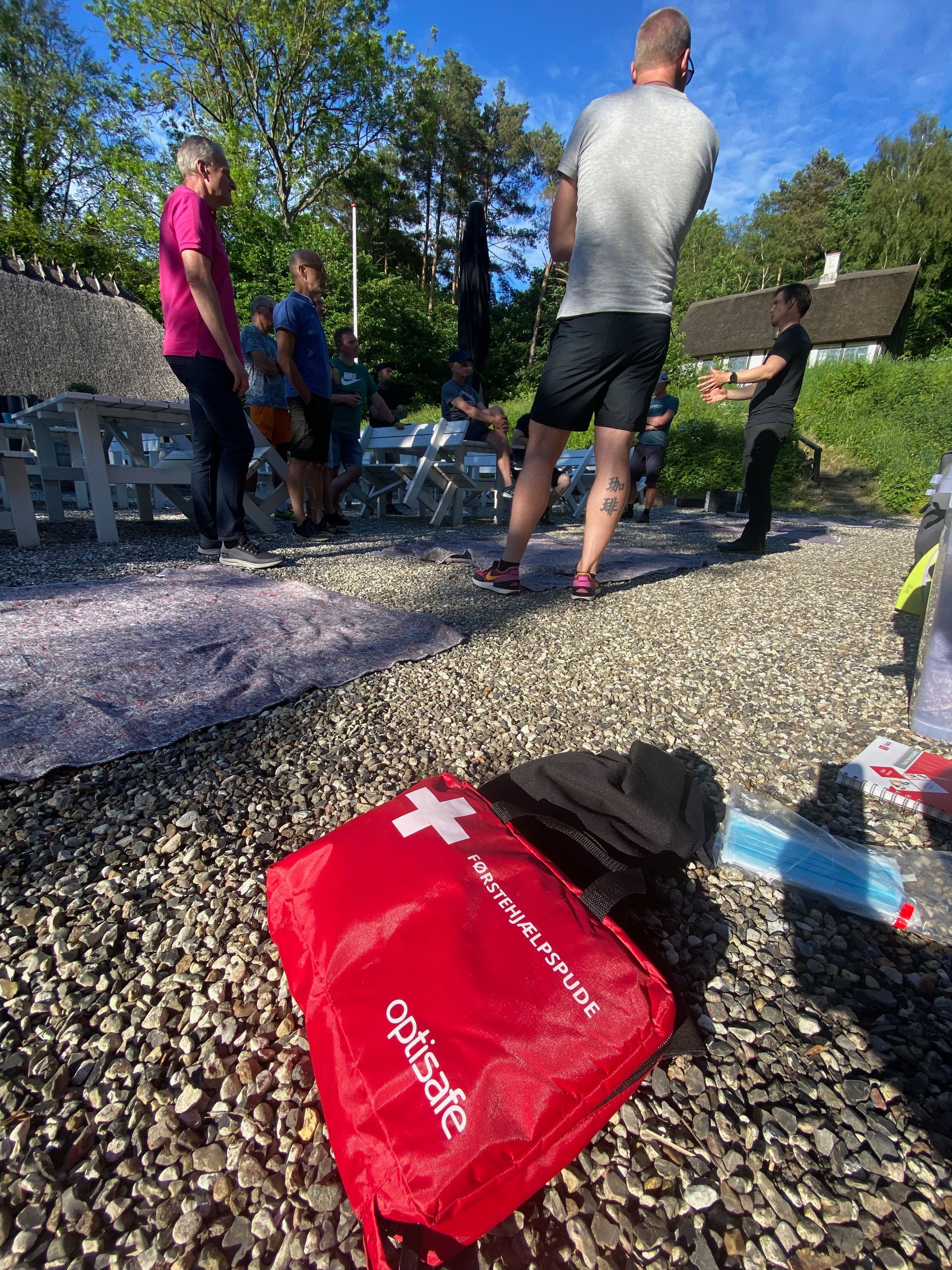 Rød førstehjælpskasse på småsten med mennesker i baggrunden.