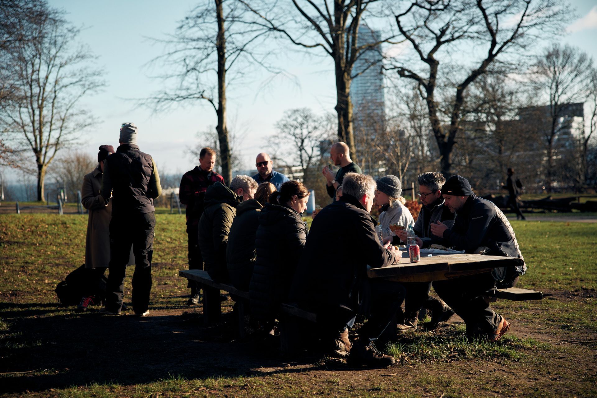 En gruppe mennesker sidder omkring et picnicbord i en park.