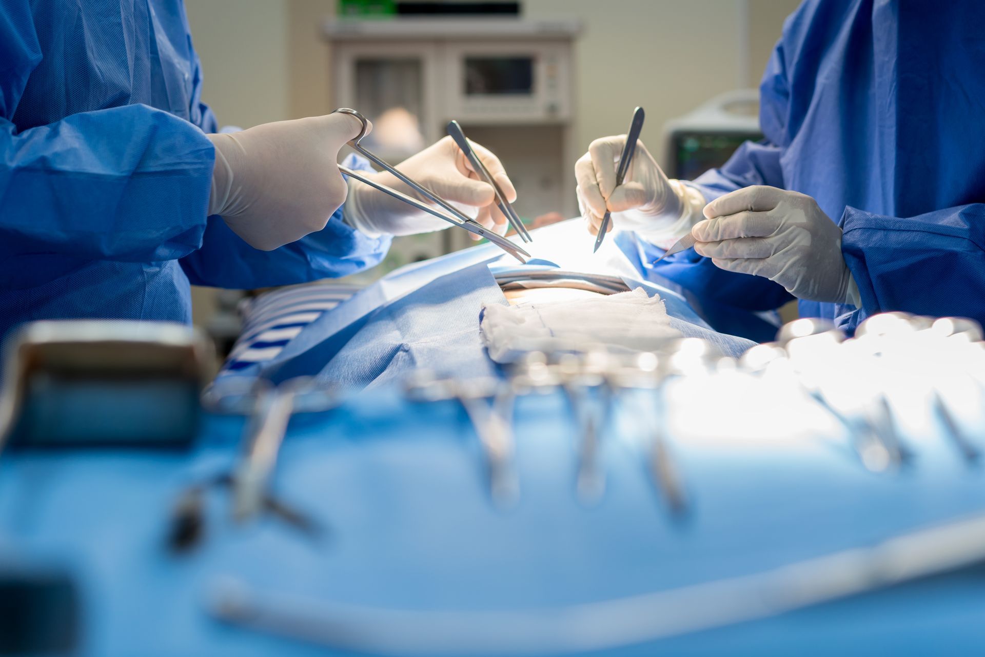 Surgeons in blue scrubs perform surgery, instruments visible on the blue draped patient.