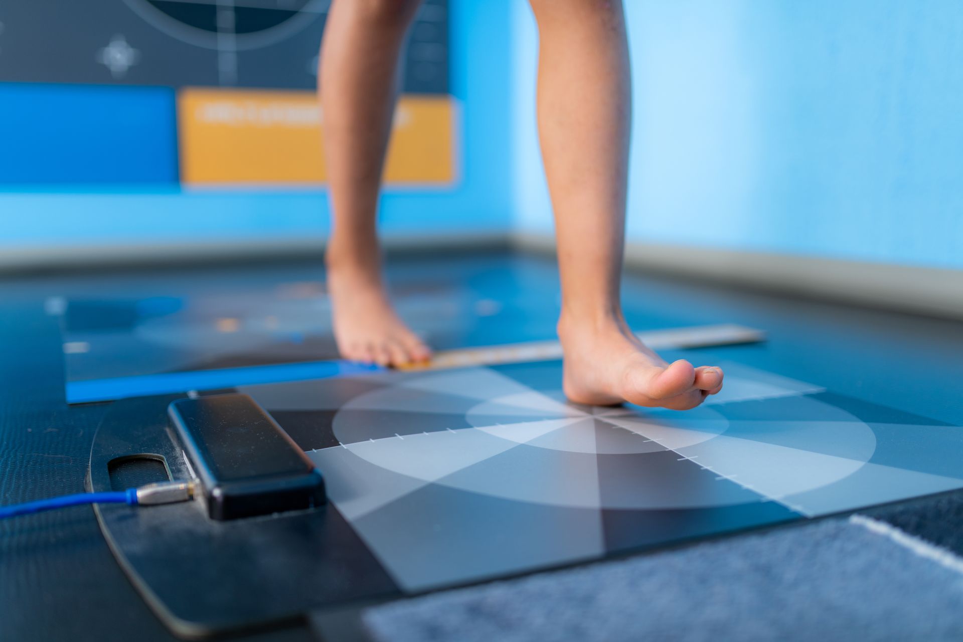 Bare feet walking on a sensor mat for gait analysis; blue and grey background.