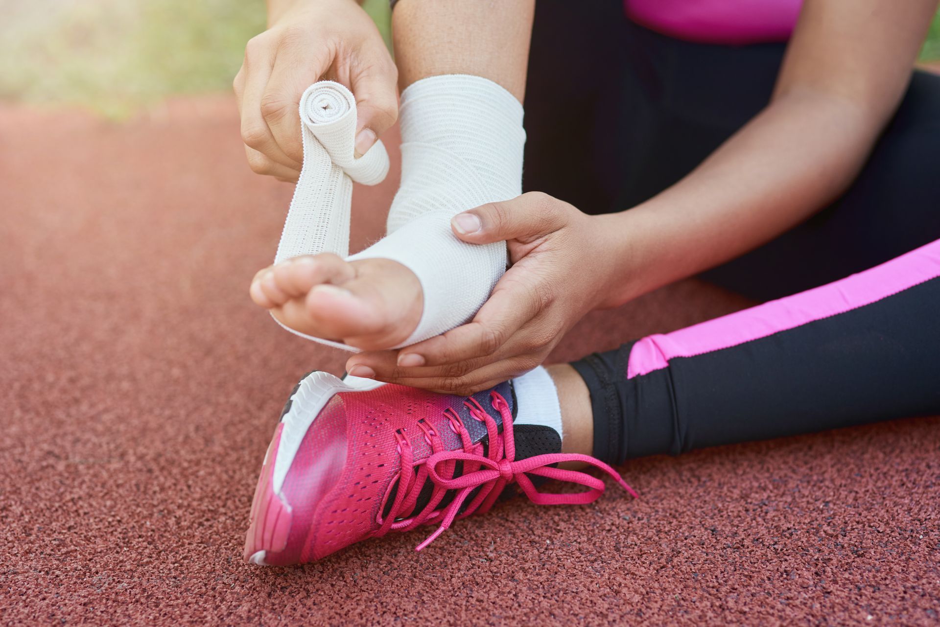 Person wrapping ankle with bandage, seated on a track.