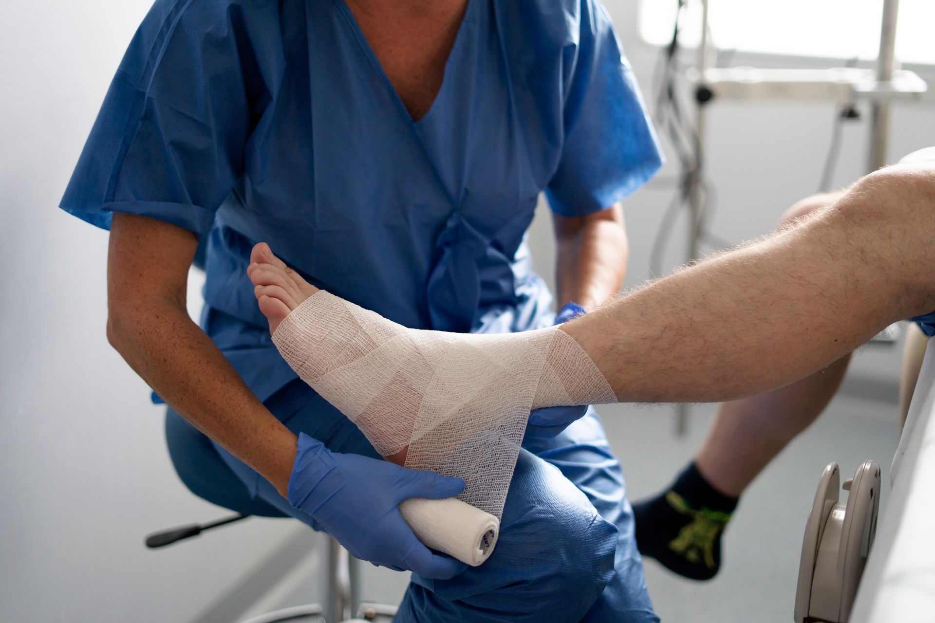 Nurse wraps a patient's foot and ankle with white bandage in a medical setting.