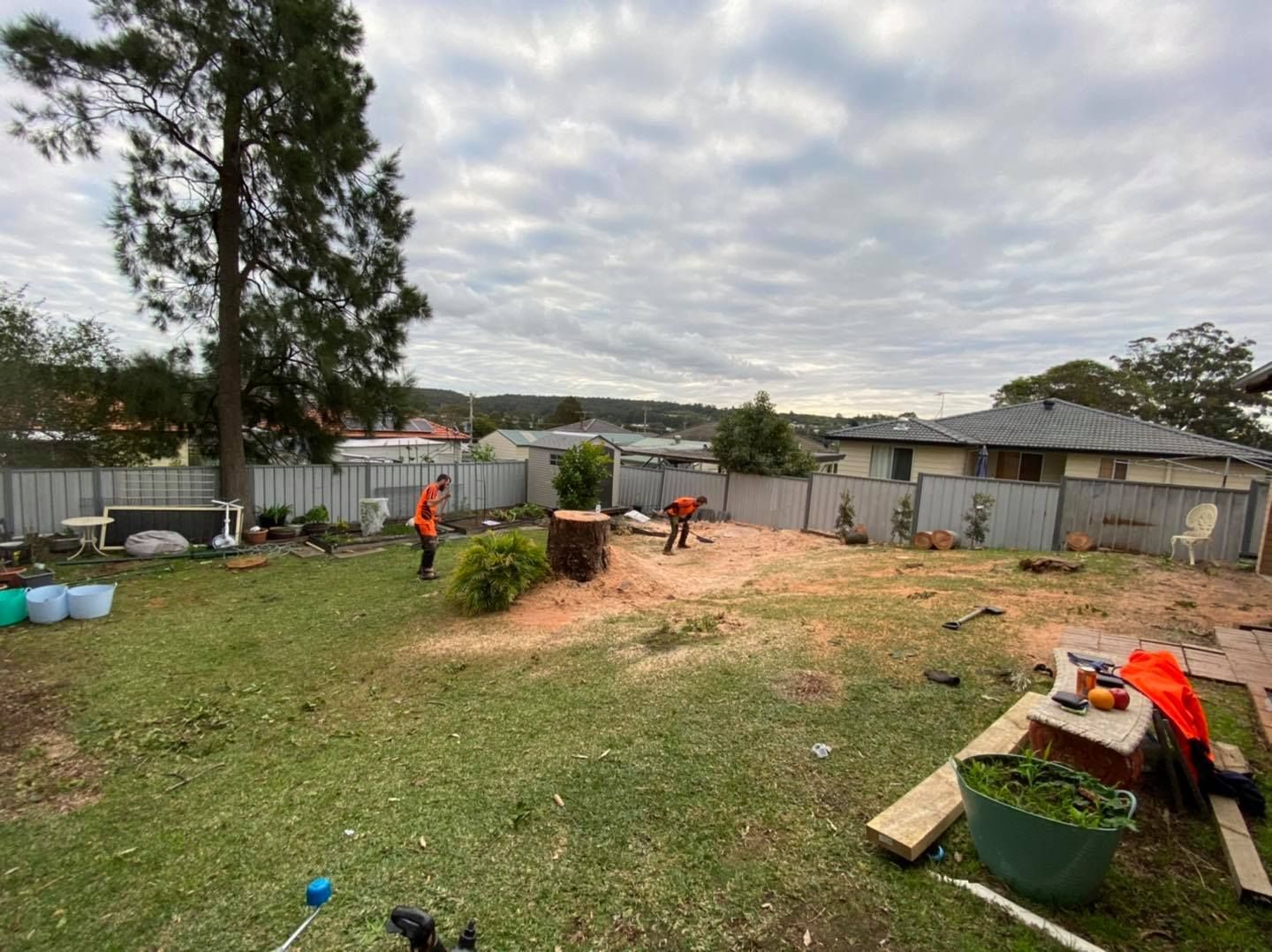 Two Tree Workers in a Backyard, Sawing a Stump on a Cloudy Day — Chop n Drop Tree Specialists in Lake Macquarie, NSW