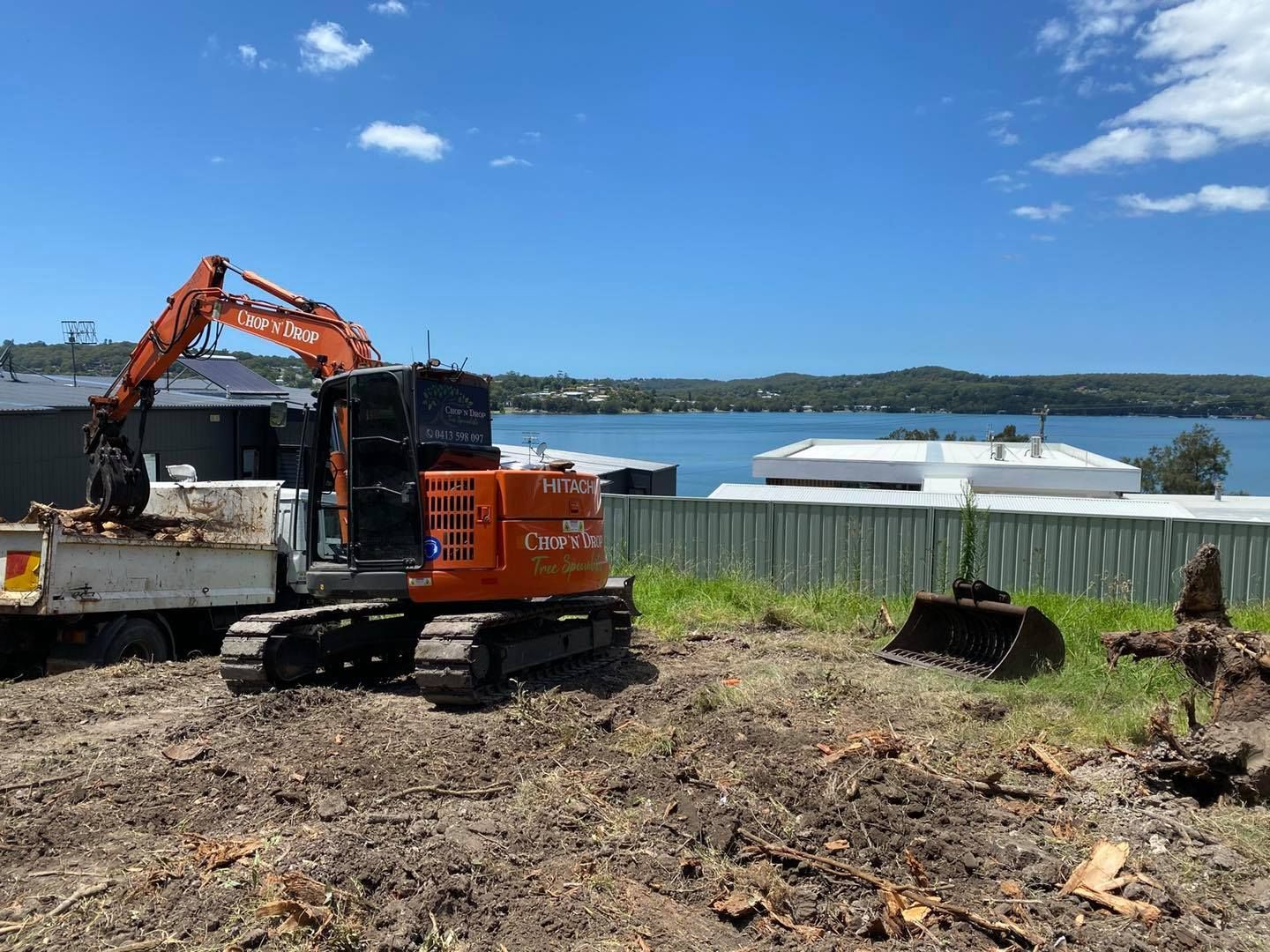 Orange Excavator Loading a Truck With Debris at a Construction Site — Chop n Drop Tree Specialists in Charlestown, NSW