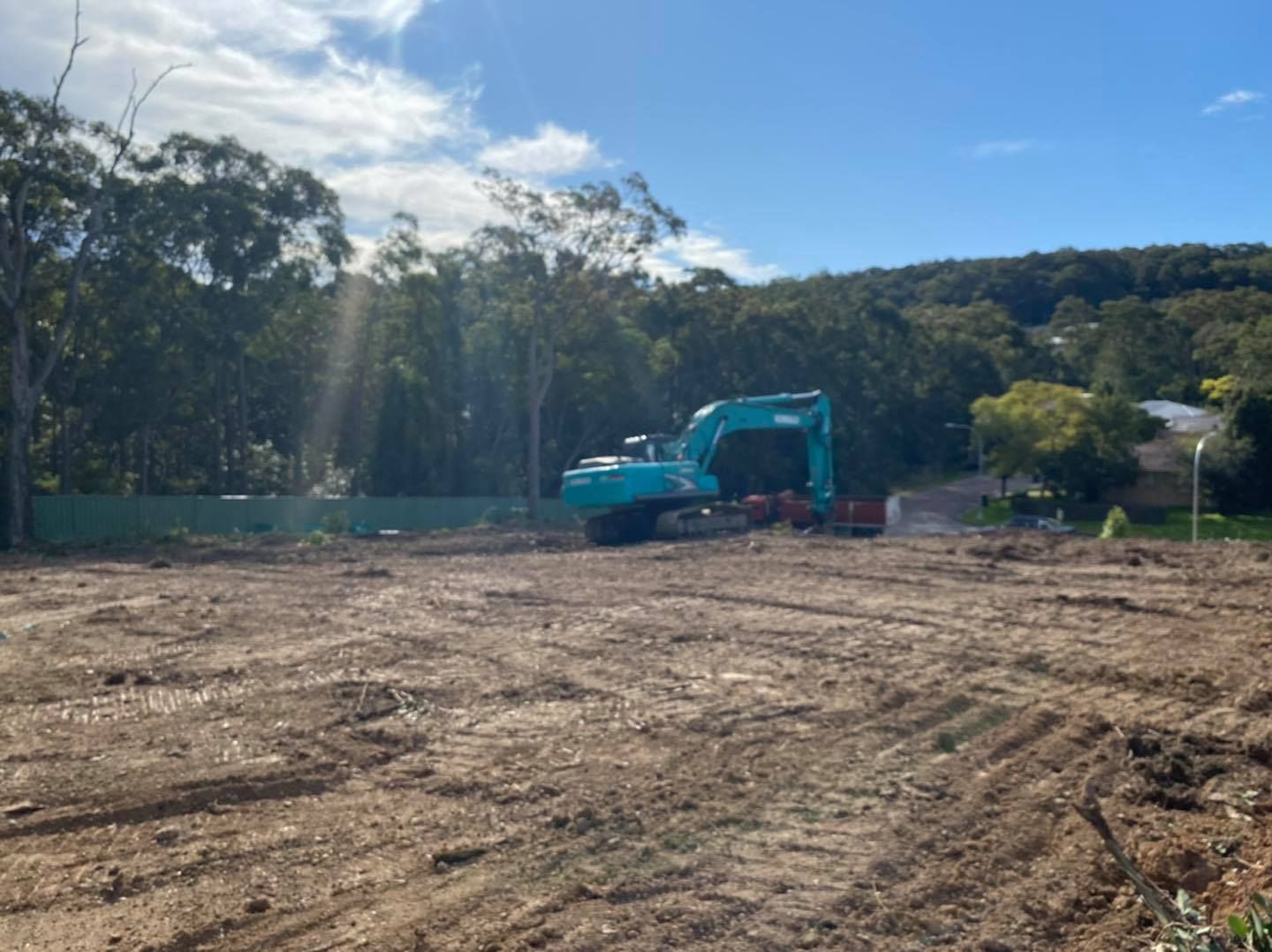 A Blue Excavator on a Cleared Construction Site With a Forest Backdrop — Chop n Drop Tree Specialists in Warners Bay, NSW