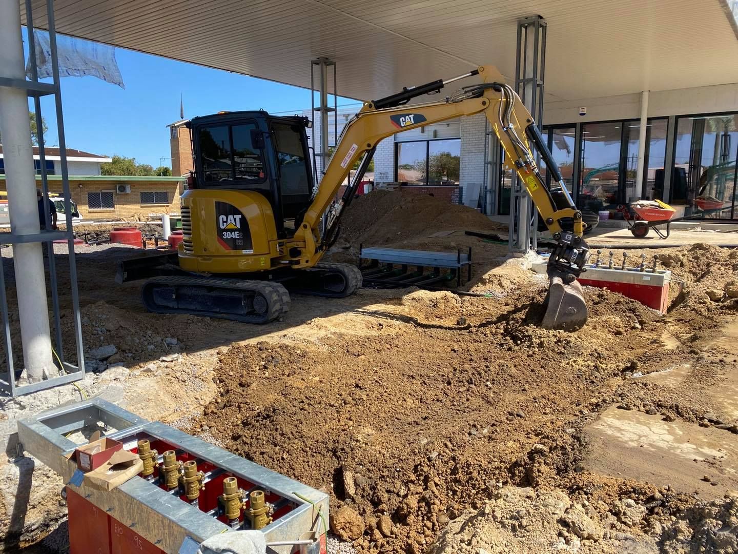 A Yellow CAT Excavator Digging in Dirt Near a Building Under Construction — Chop n Drop Tree Specialists in Belmont, NSW