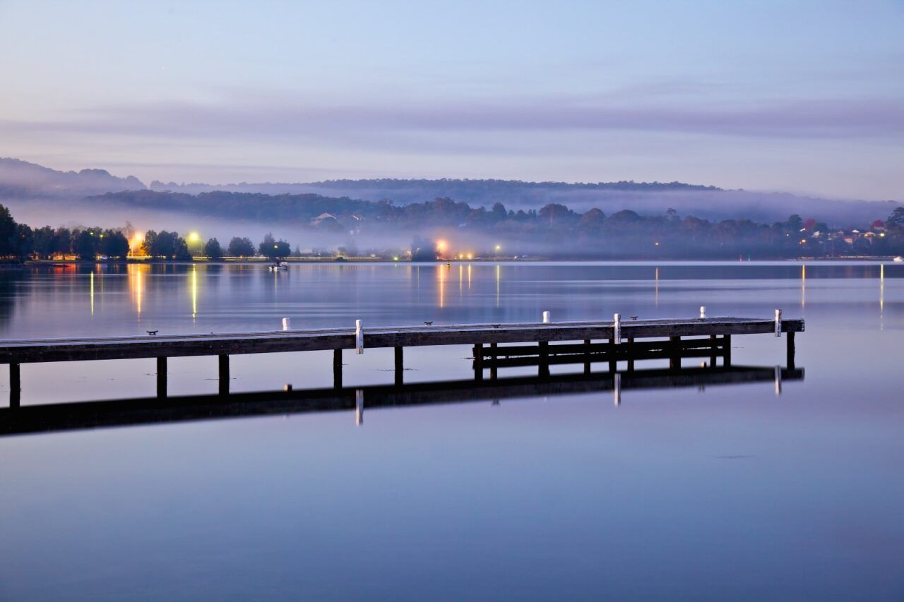 Wooden Dock Extending Into a Still Lake at Dusk — Chop n Drop Tree Specialists in Warners Bay, NSW