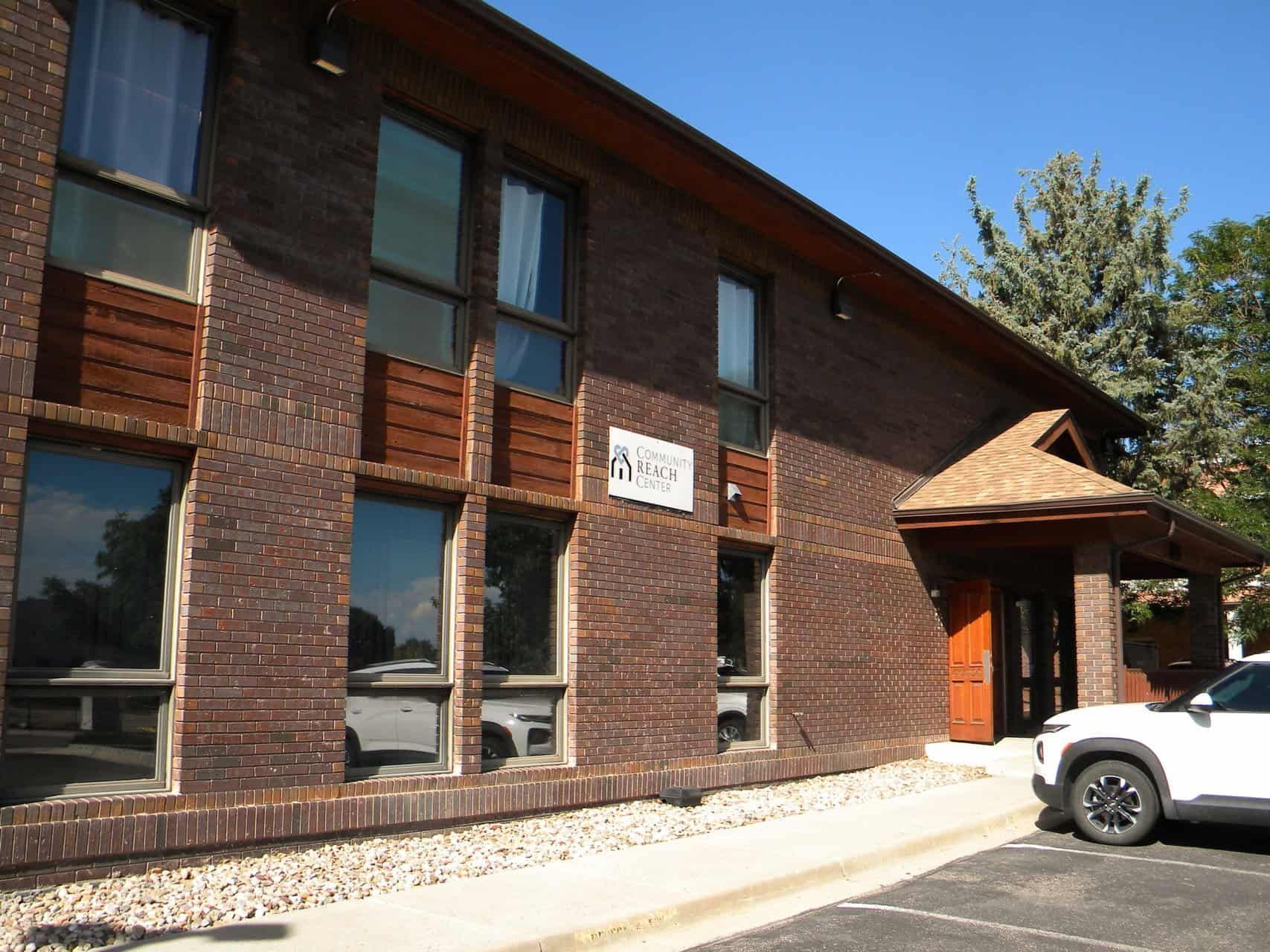 Brick building with windows, a covered entryway, and a parked SUV.