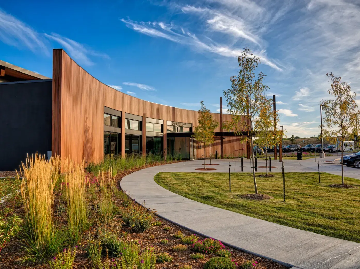 Curved building with rust-colored exterior, sidewalk, and landscaping under a blue sky.
