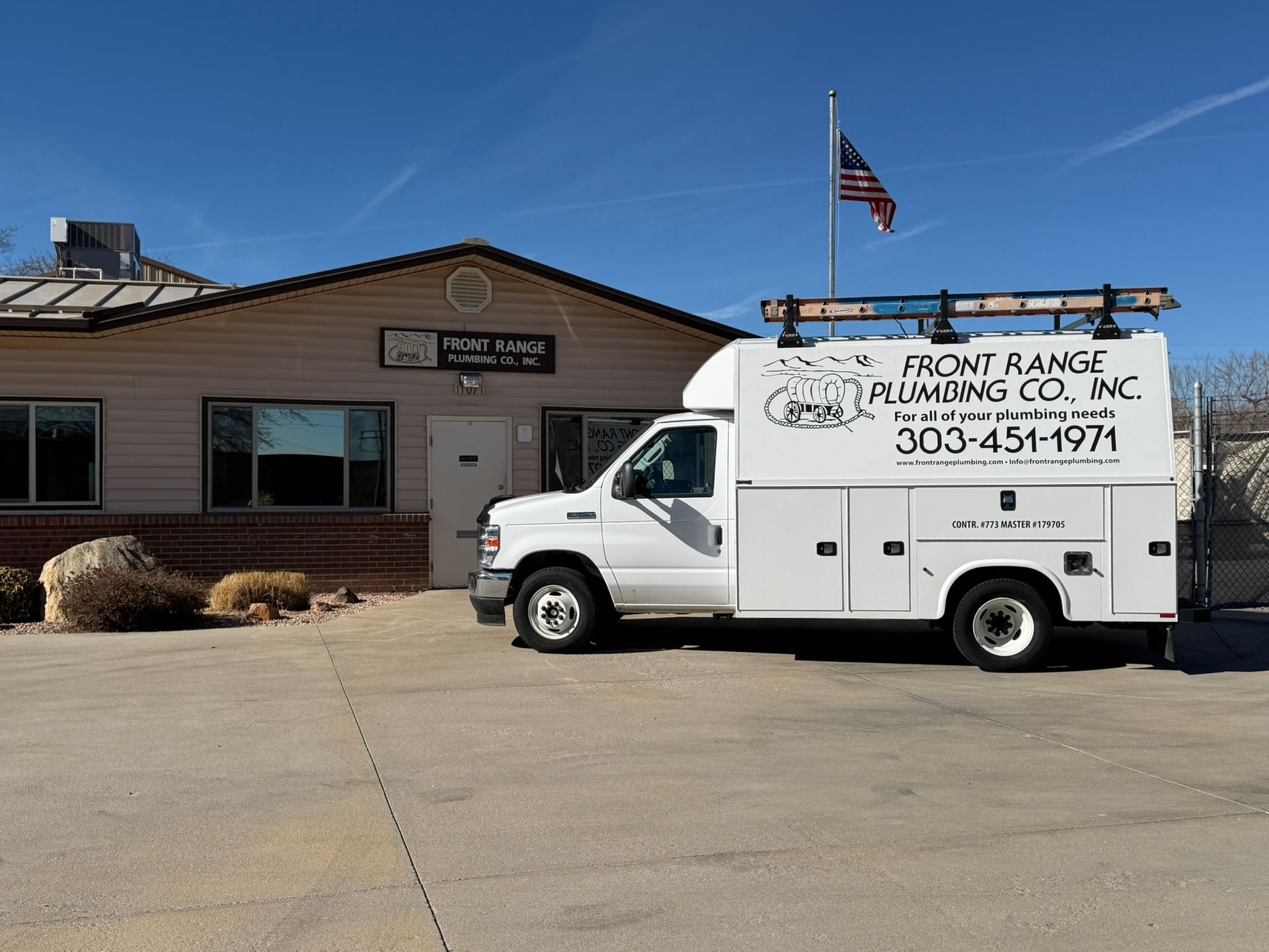 White plumbing truck parked in front of a building with an American flag. 
