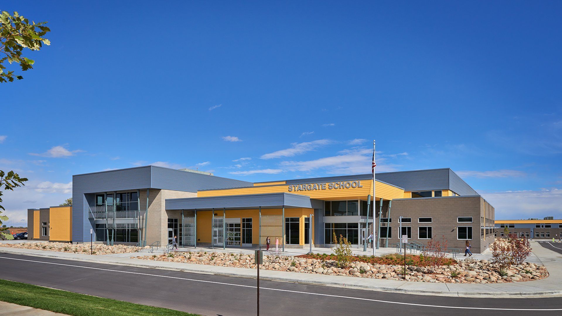 Modern school building with gray and yellow accents under a blue sky.