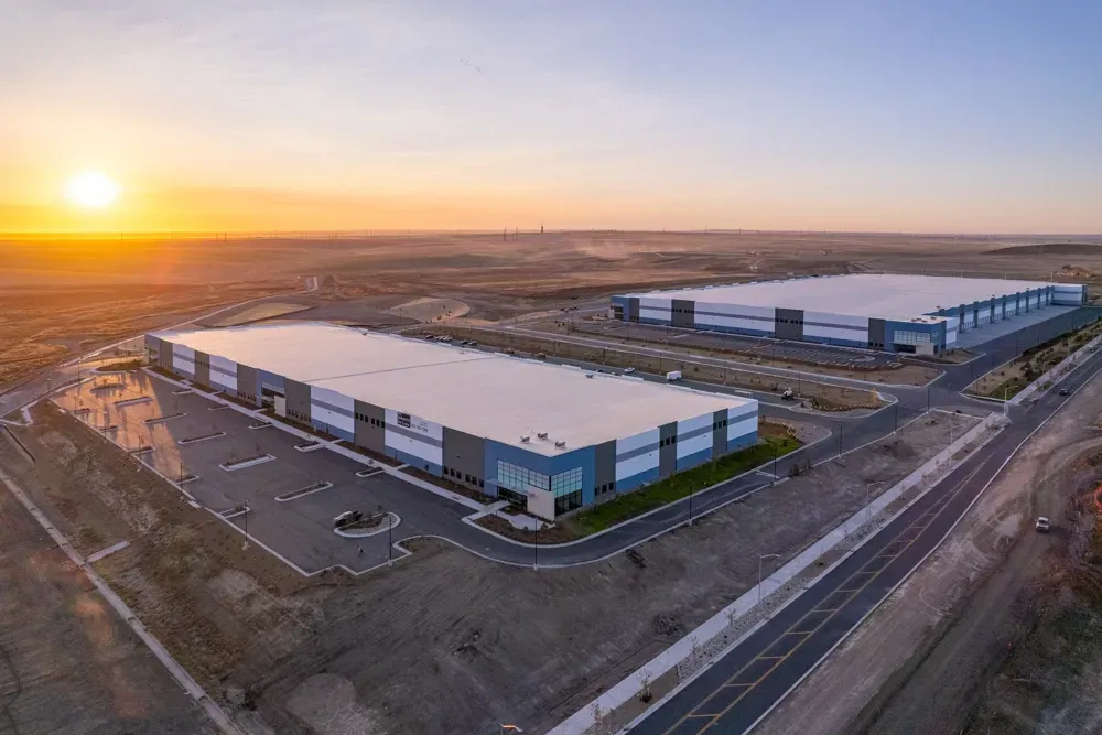 Two large industrial buildings at sunset, with vast, open land.