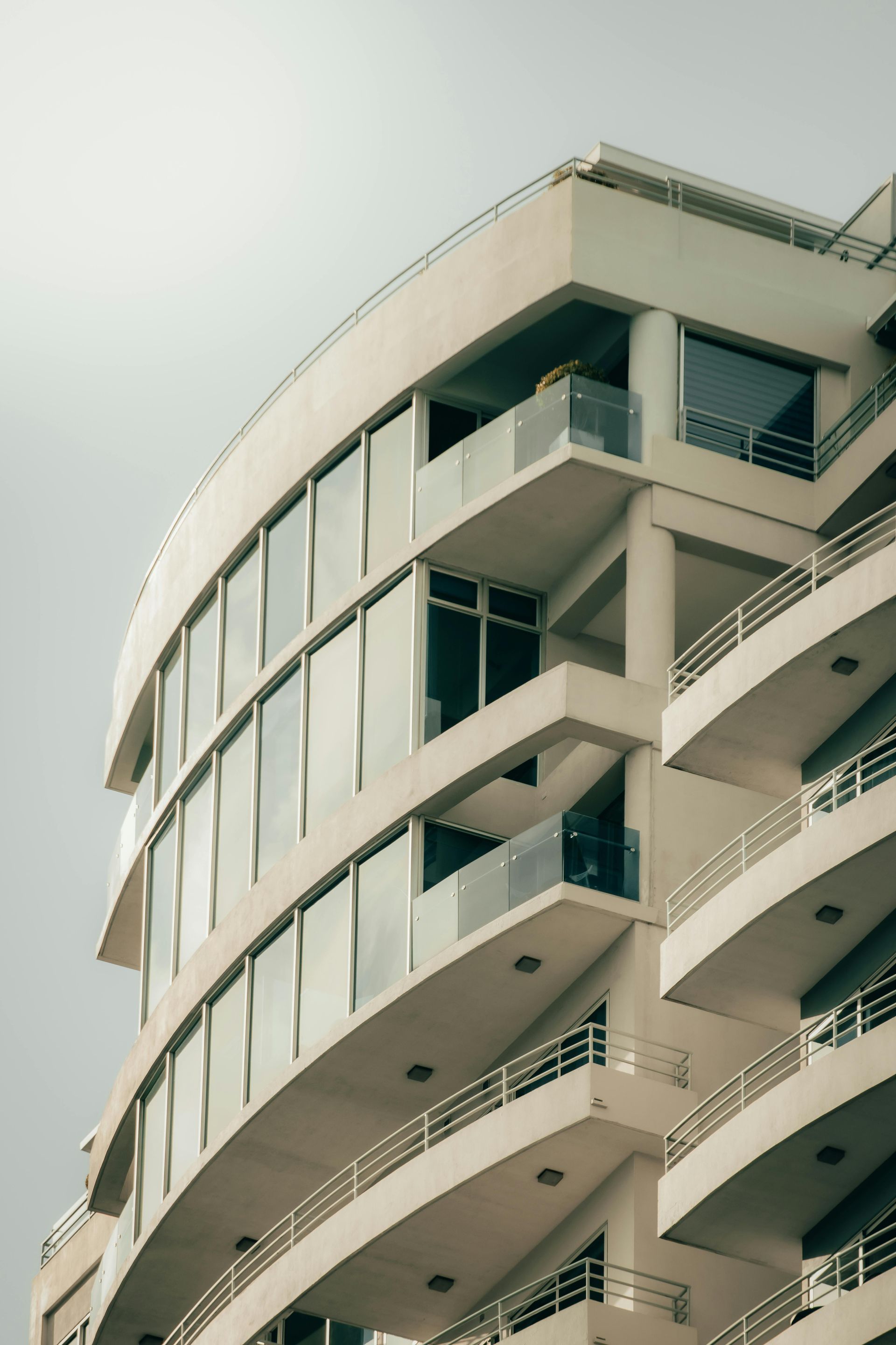 Curved, white modern building with balconies and large windows against a grey sky.