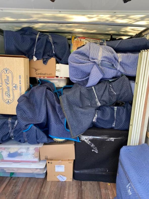 A view inside a moving truck packed with furniture covered in blue moving blankets and various cardboard boxes.