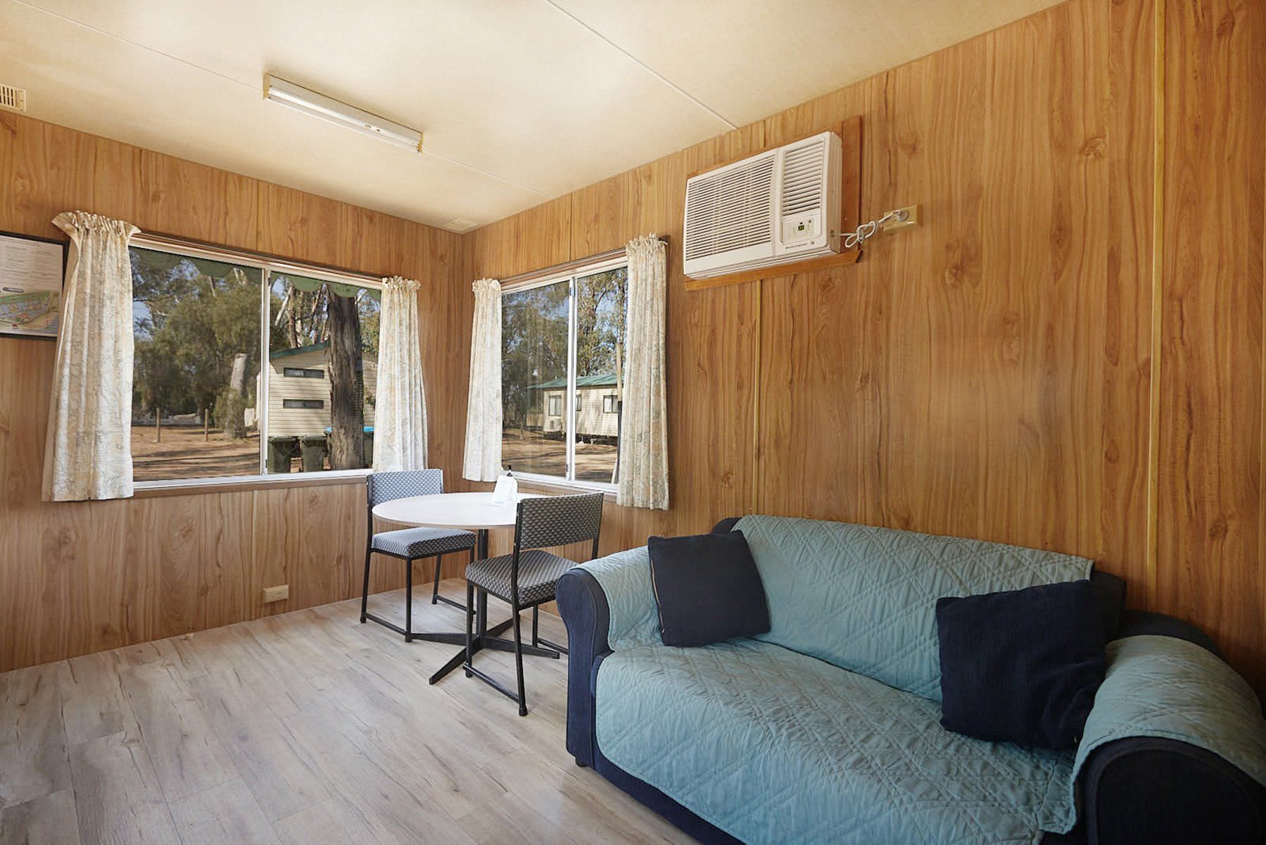 Apex Riverbeach Holiday Park cabin's lounge room with a sofa couch , table and chairs , trees in the background .