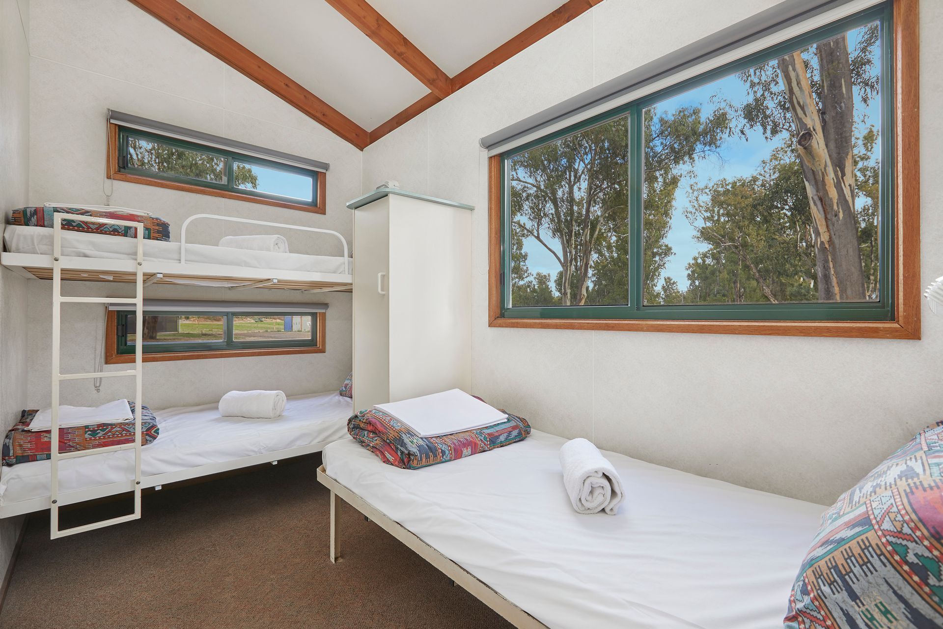 Apex Riverbeach Holiday Park cabin's bedroom with three bunk beds and windows .