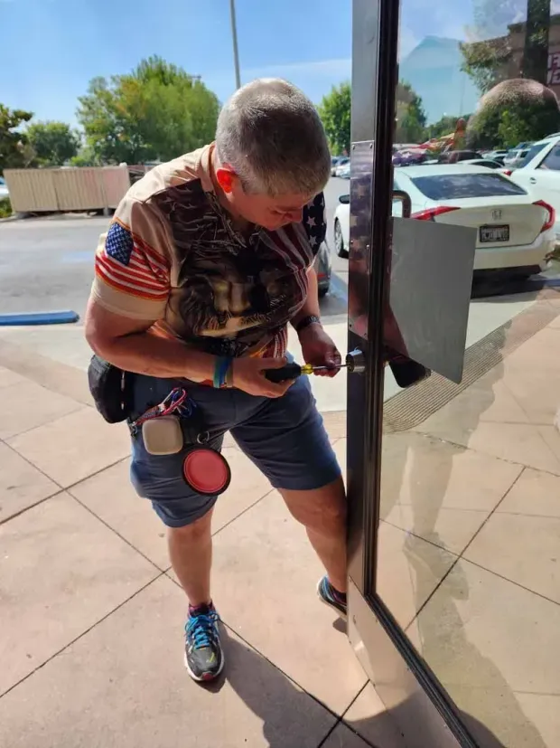 A man is standing in front of a glass door looking at his phone.