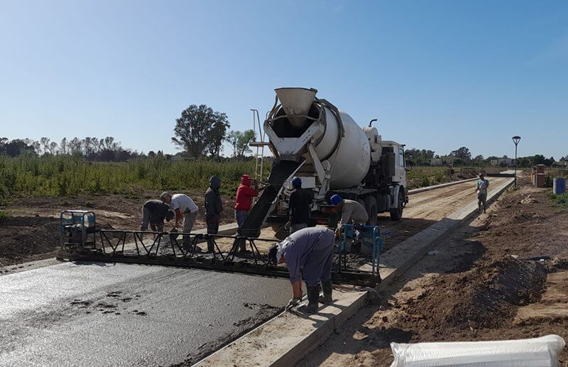 Los obreros de la construcción utilizan una hormigonera para verter y nivelar el hormigón fresco para una nueva superficie de carretera bajo un cielo azul despejado.