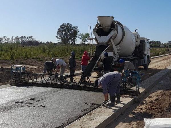 Un camión hormigonera vierte cemento fresco sobre la superficie de una carretera mientras los trabajadores de la construcción utilizan herramientas para nivelarla al aire libre.
