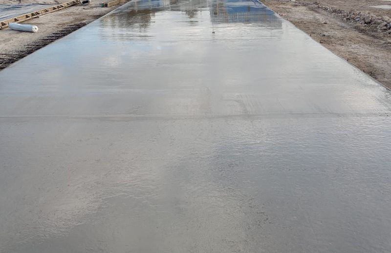 Losa de hormigón gris recién vertida en una obra en construcción, con una superficie lisa, húmeda y reflectante.