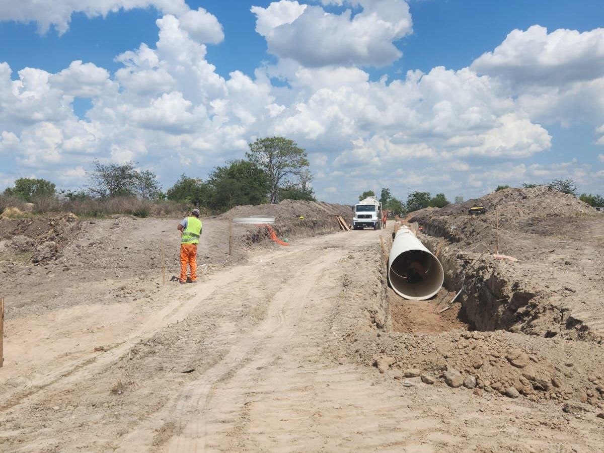 Un trabajador con ropa de alta visibilidad se encuentra cerca de una zanja abierta con una tubería grande en una obra de construcción al aire libre.