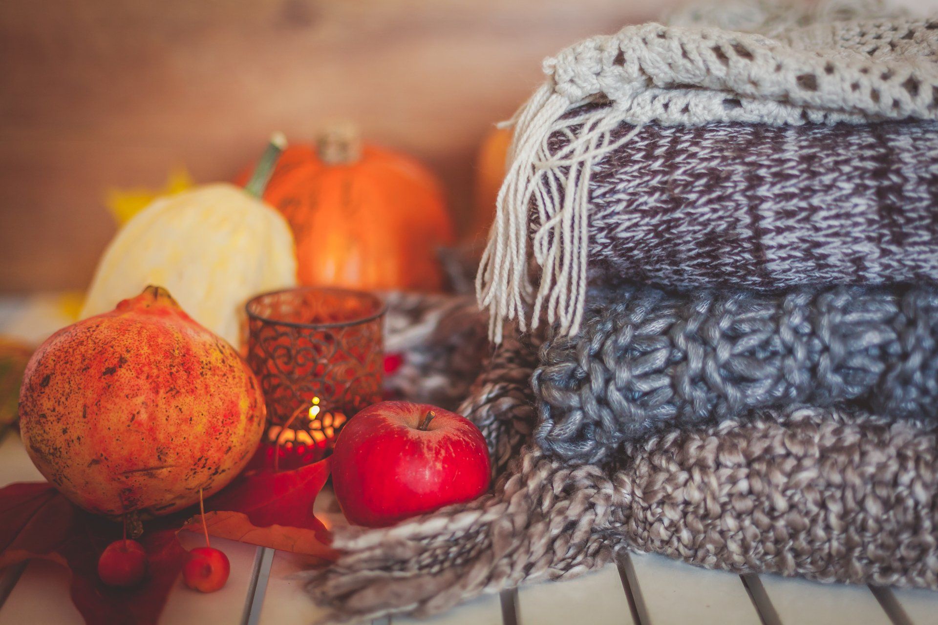 Cosy stack of blankets, candle, pumpkins & fall fruit