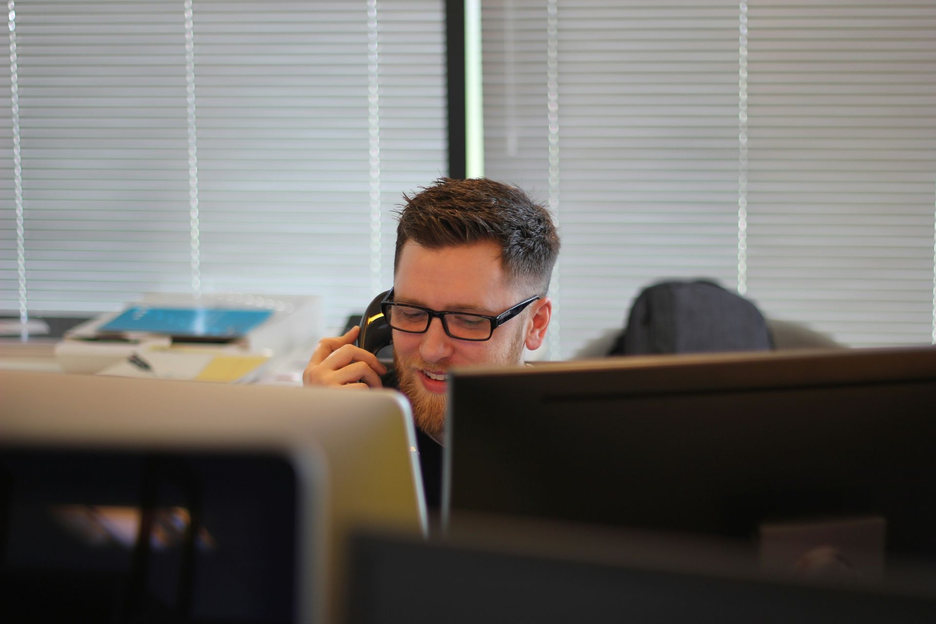 Man in glasses smiles while talking on a phone with customers