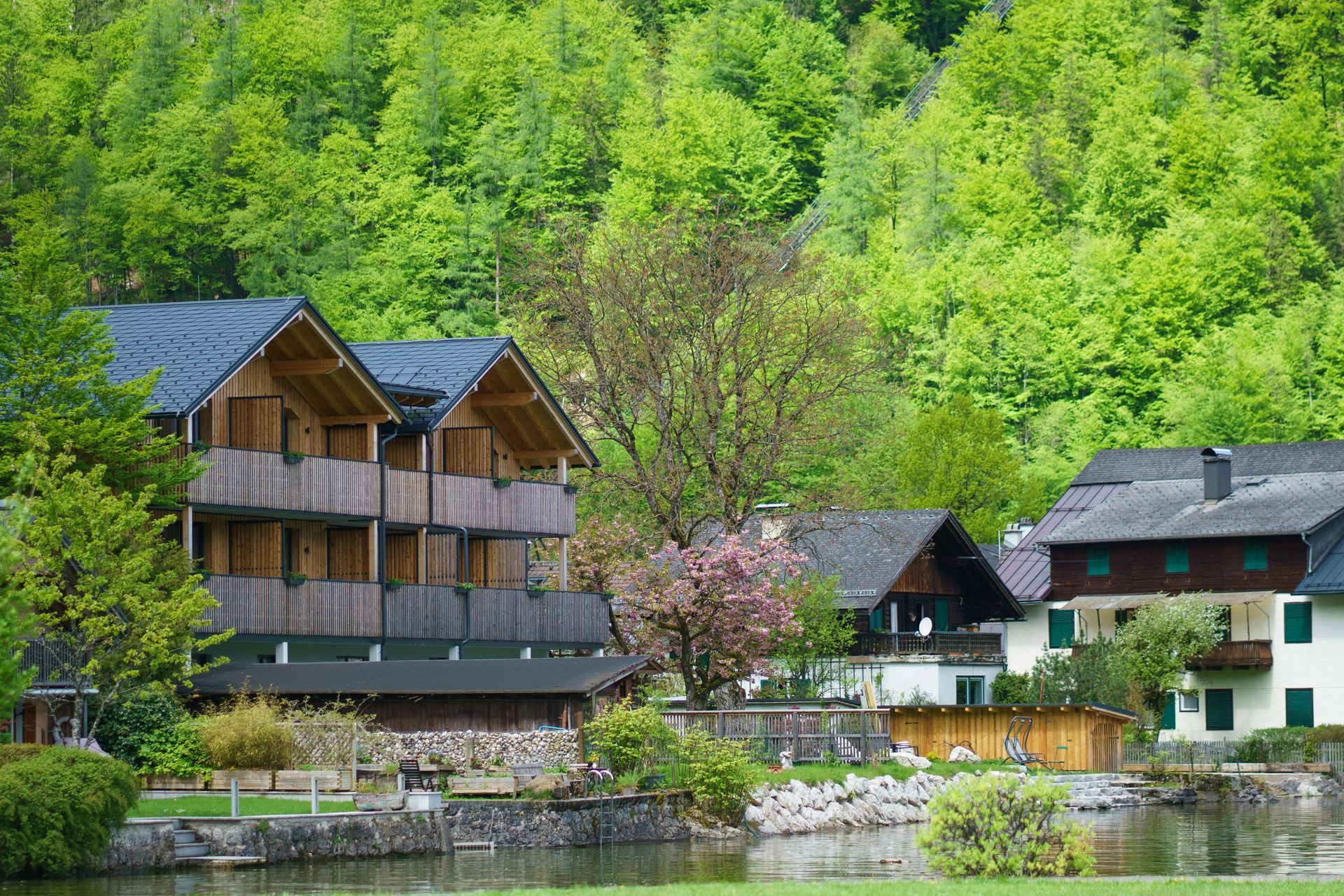 Wooden lakeside cabins in a lush green forest with mountains behind