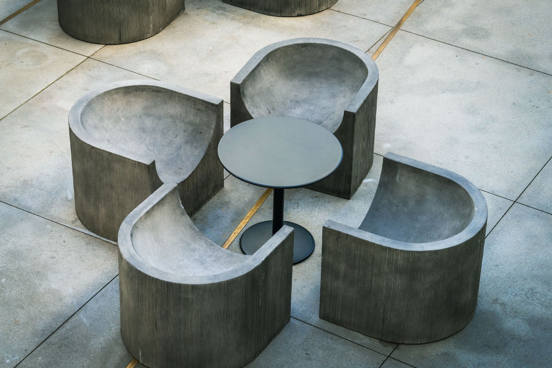 Abstract concrete outdoor seating with curved gray benches around a small round table on tiled pavement