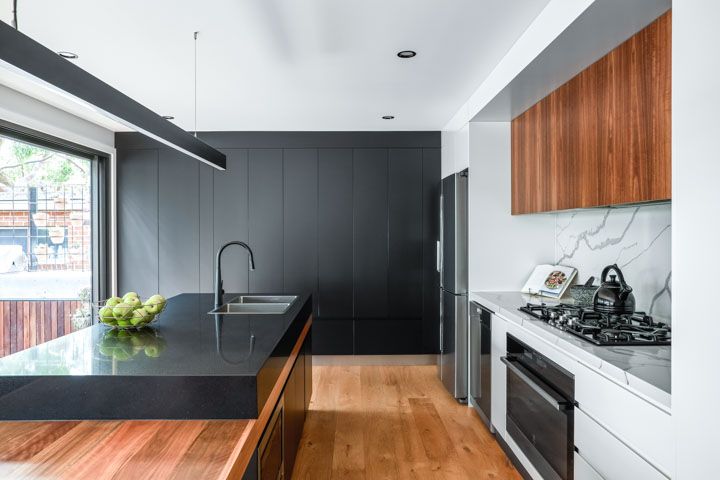 A kitchen with black cabinets and wooden floors and a large island in the middle.