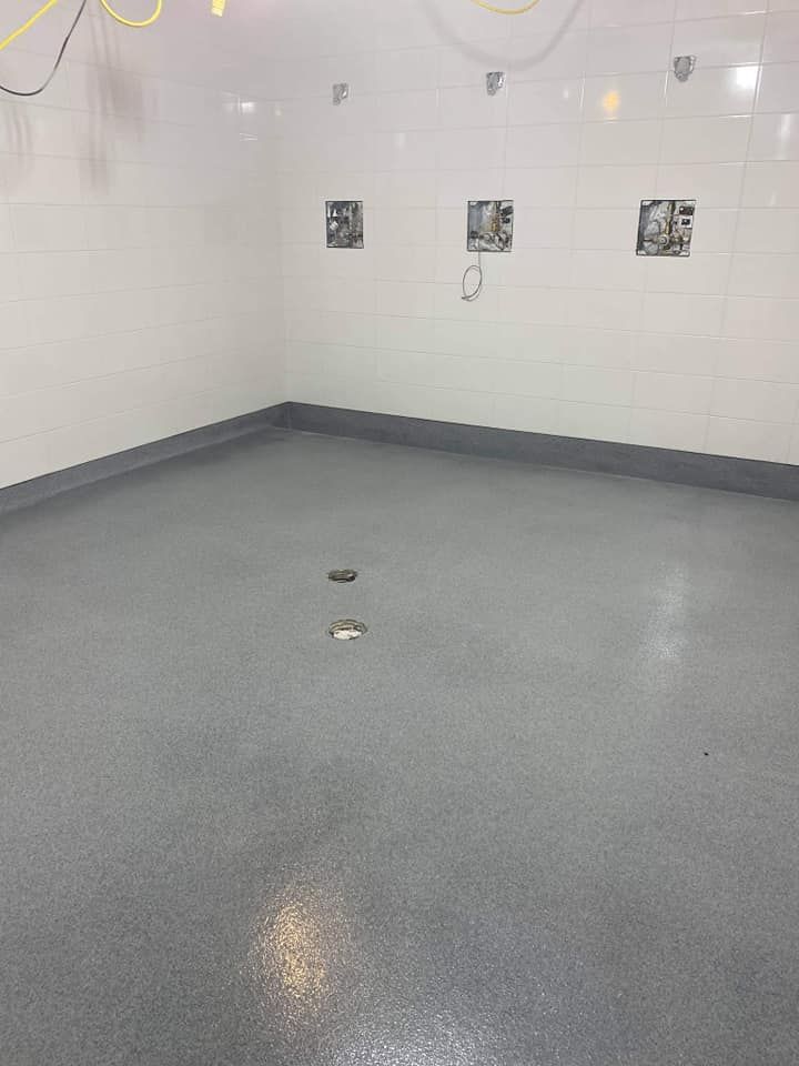 Une grande pièce vide avec un sol gris et des murs blancs.