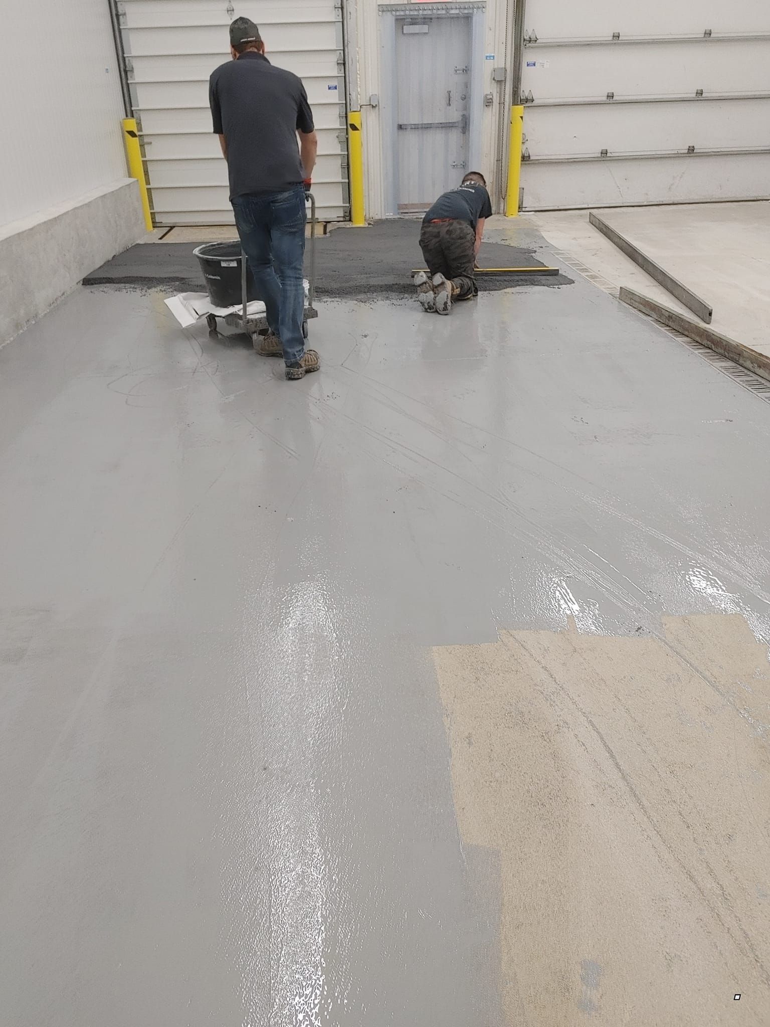 Deux hommes peignent un sol en béton dans un garage.