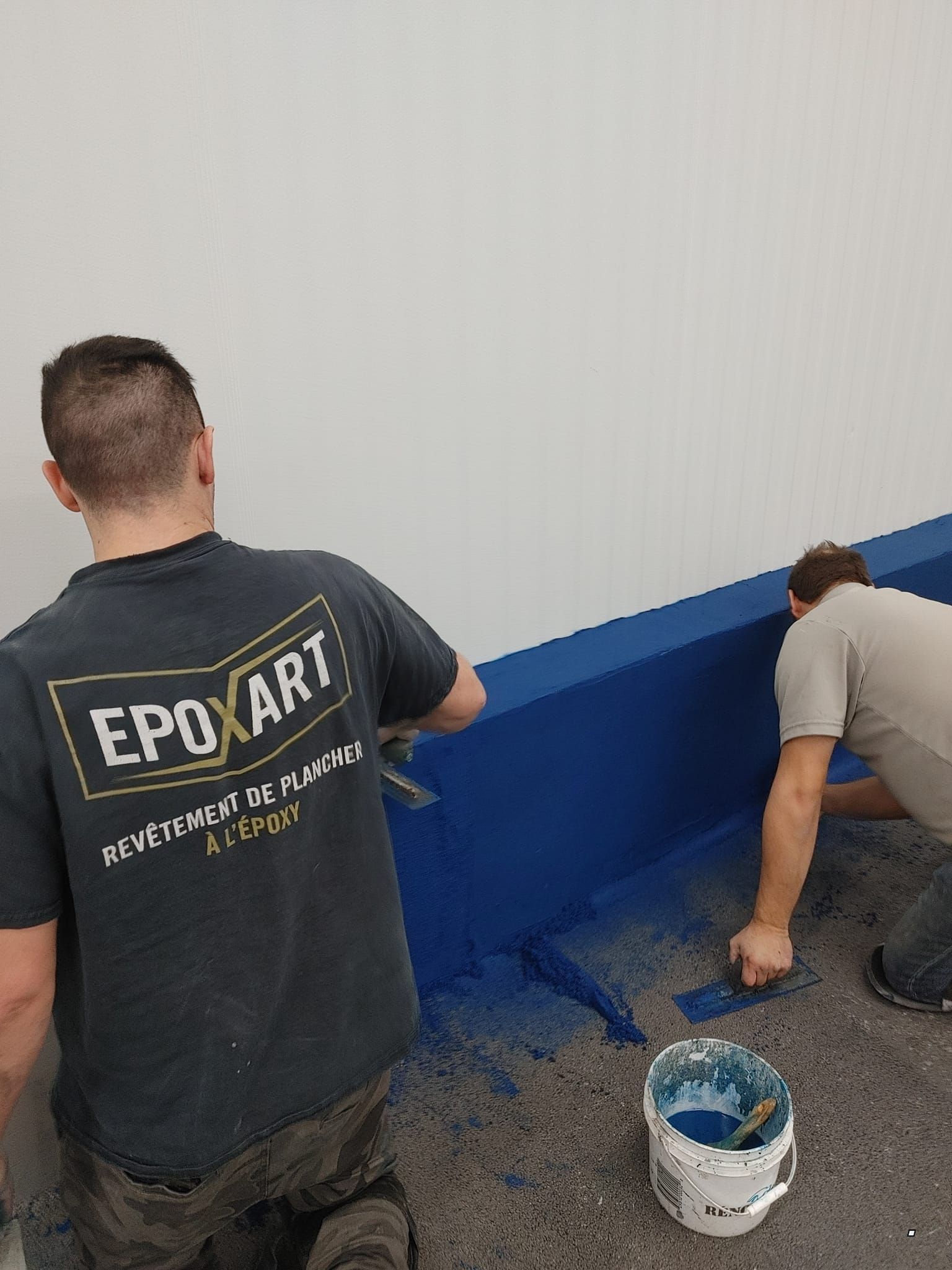 Deux hommes peignent un mur avec de la peinture bleue.