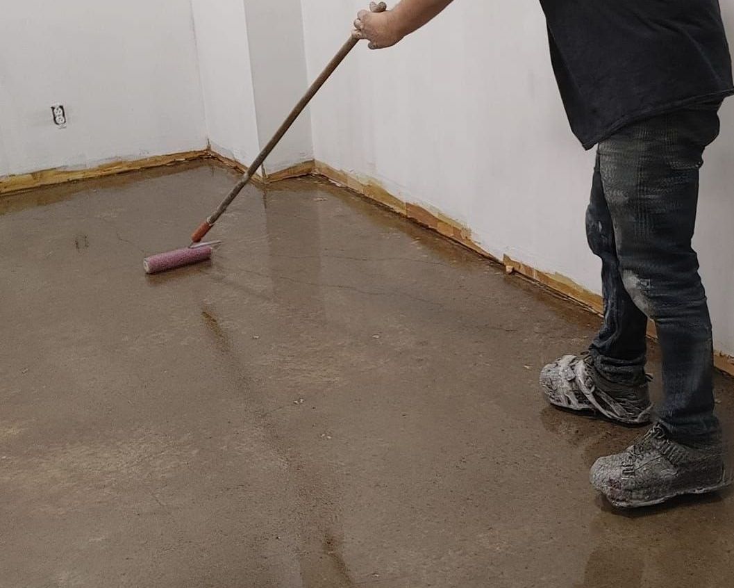 Un homme utilise un rouleau pour étaler du béton sur un sol.
