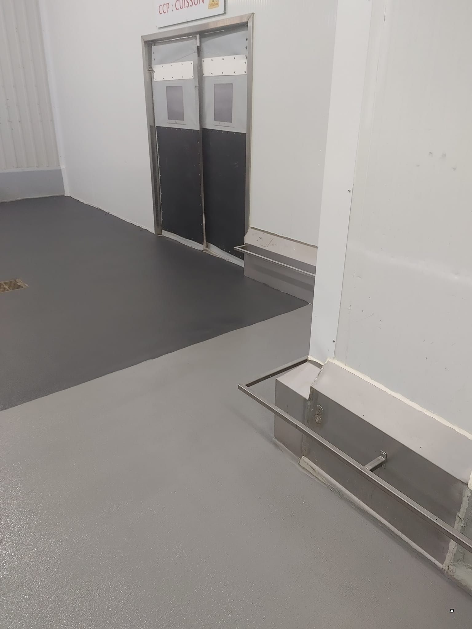 Une pièce avec une porte noire et un sol gris.