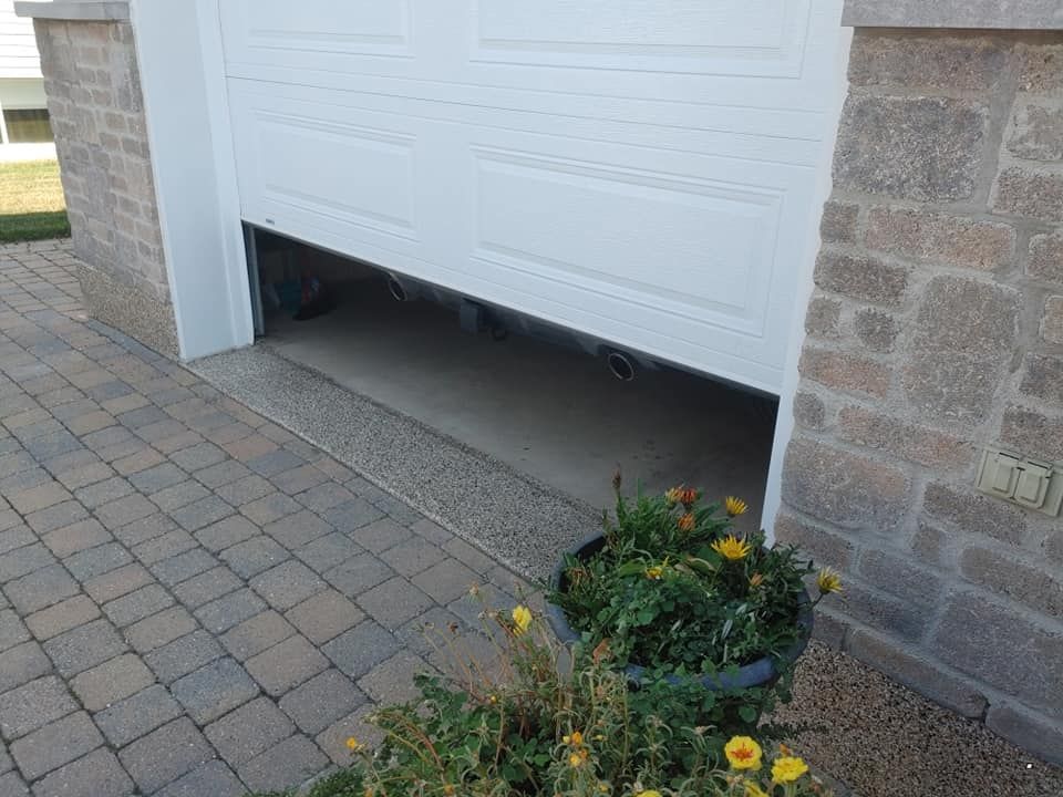 Une porte de garage blanche est ouverte et un pot de fleurs se trouve devant elle.