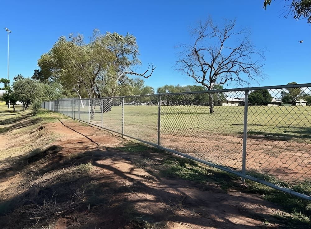 A Chain Link Fence Surrounds A Field With Trees — PH Davie in Mount Isa, QLD