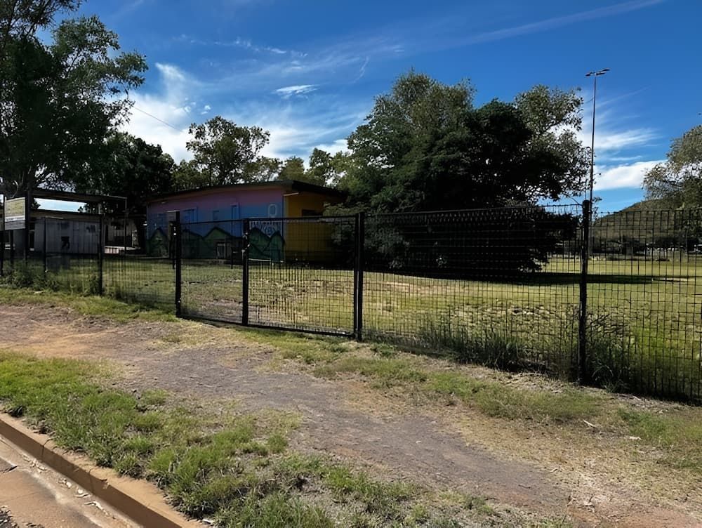 A Fence Surrounds A Grassy Field With A Building With Gate — PH Davie in Mount Isa, QLD