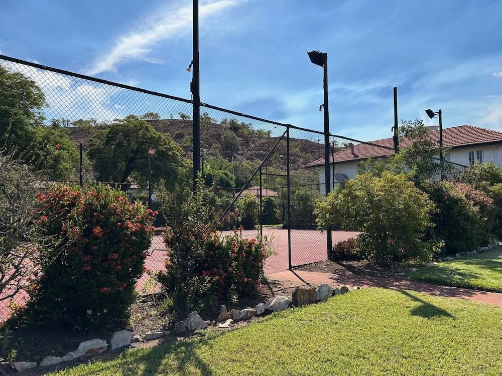A Tennis Court Is Surrounded By A Fence And Trees — PH Davie in Mount Isa, QLD