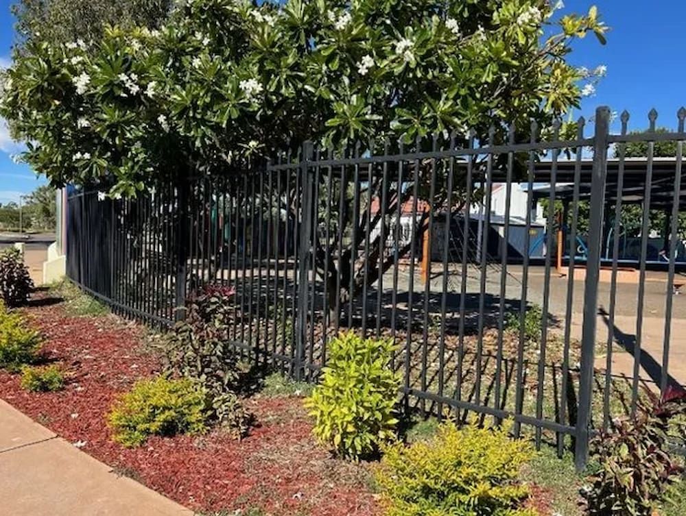 A Black Metal Fence Surrounds A Garden With A Tree — PH Davie in Mount Isa, QLD