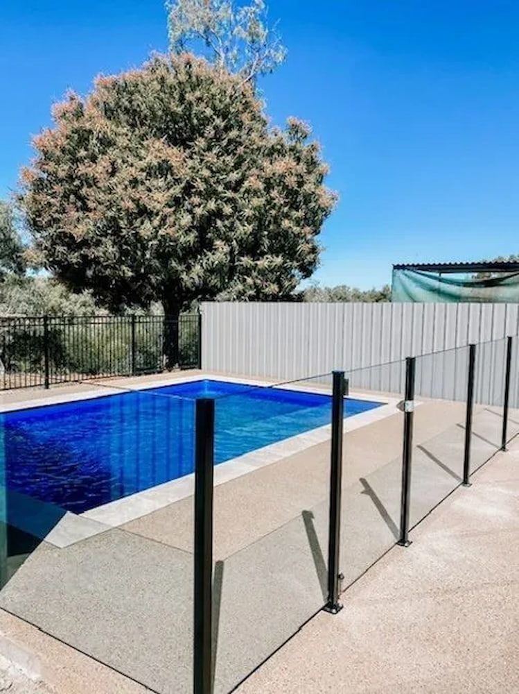 A Large Swimming Pool Surrounded By A Glass Fence With A Tree — PH Davie in Mount Isa, QLD