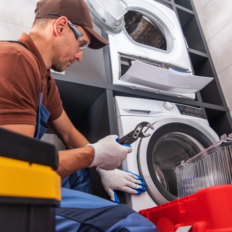 Un technicien répare une machine à laver à l'aide d'une clé, portant des lunettes de sécurité et des gants.