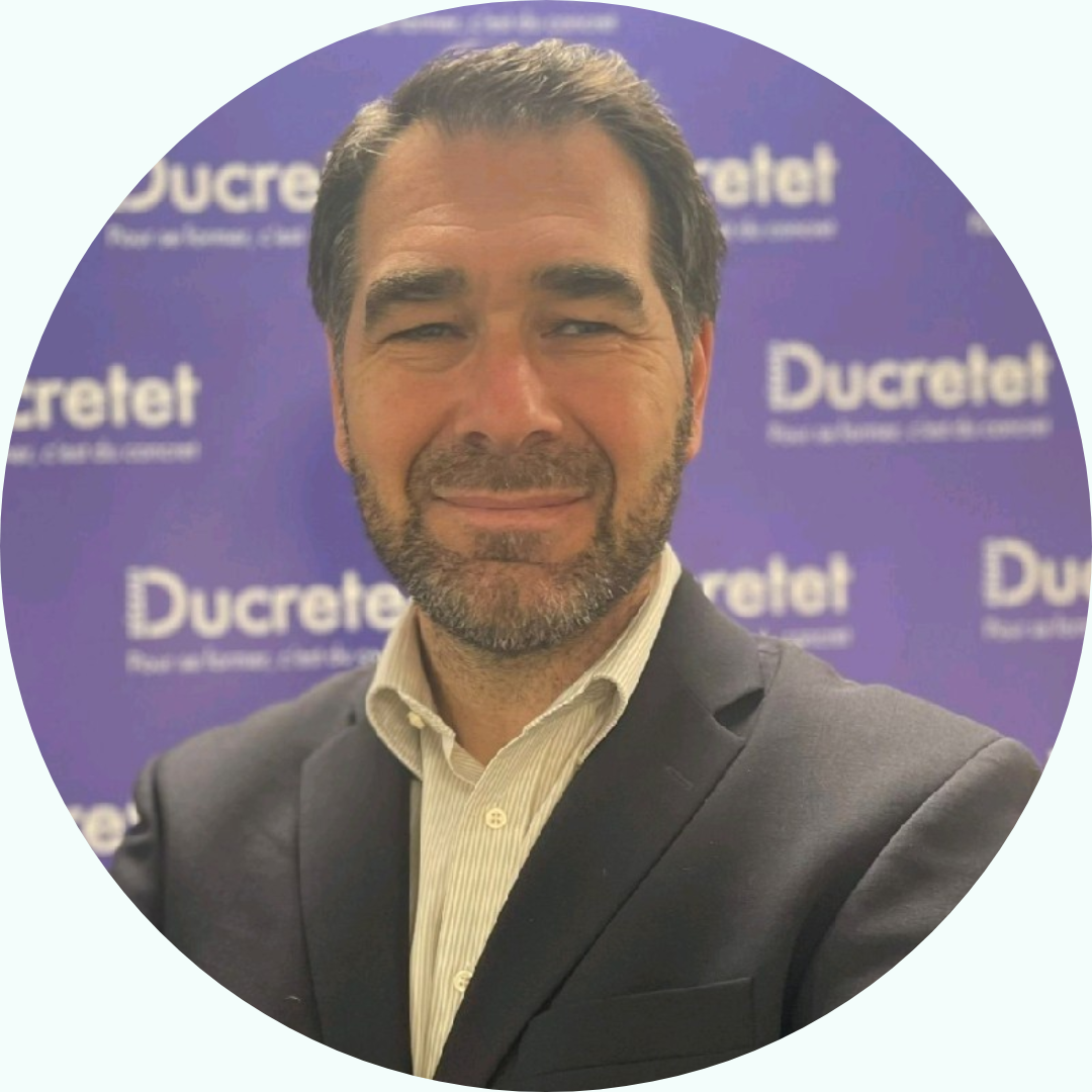 Un homme en costume sourit devant un fond violet Ducetret.