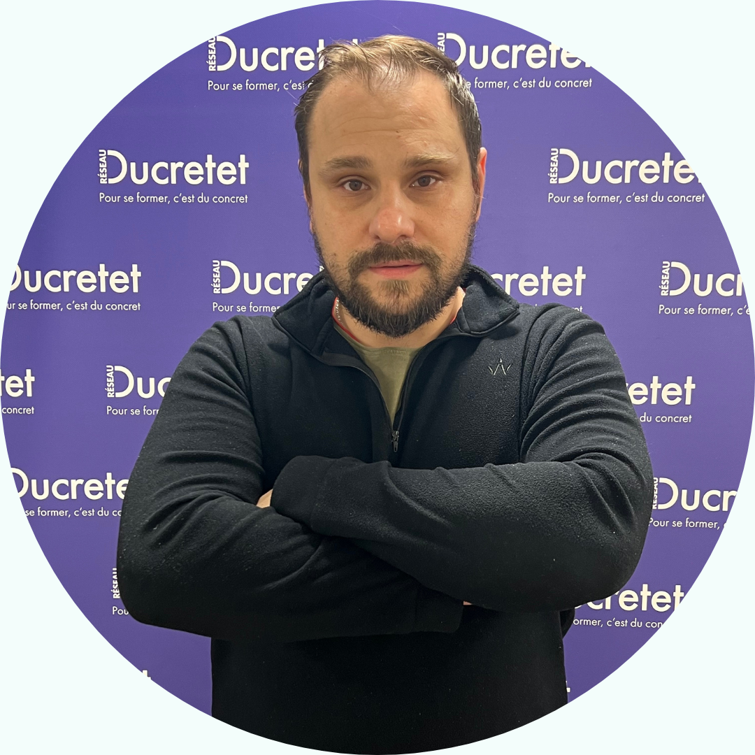 Homme aux bras croisés devant un fond violet avec le mot « Ducretet » affiché à plusieurs reprises.