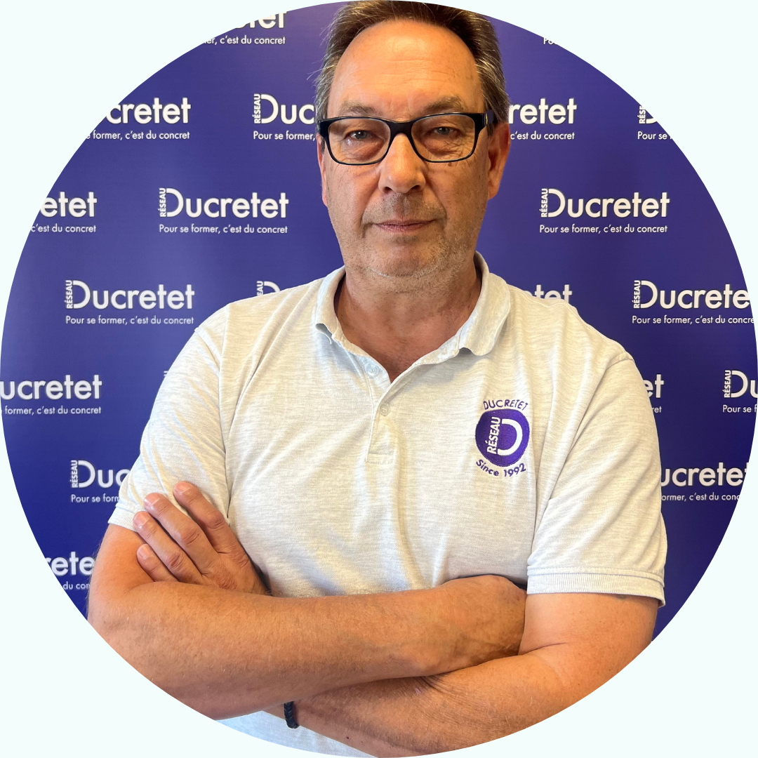 Homme portant des lunettes et les bras croisés, vêtu d'un polo gris clair siglé 