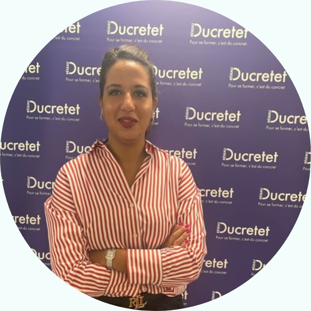 Femme aux bras croisés, vêtue d'une chemise rayée, devant un fond Ducretet.