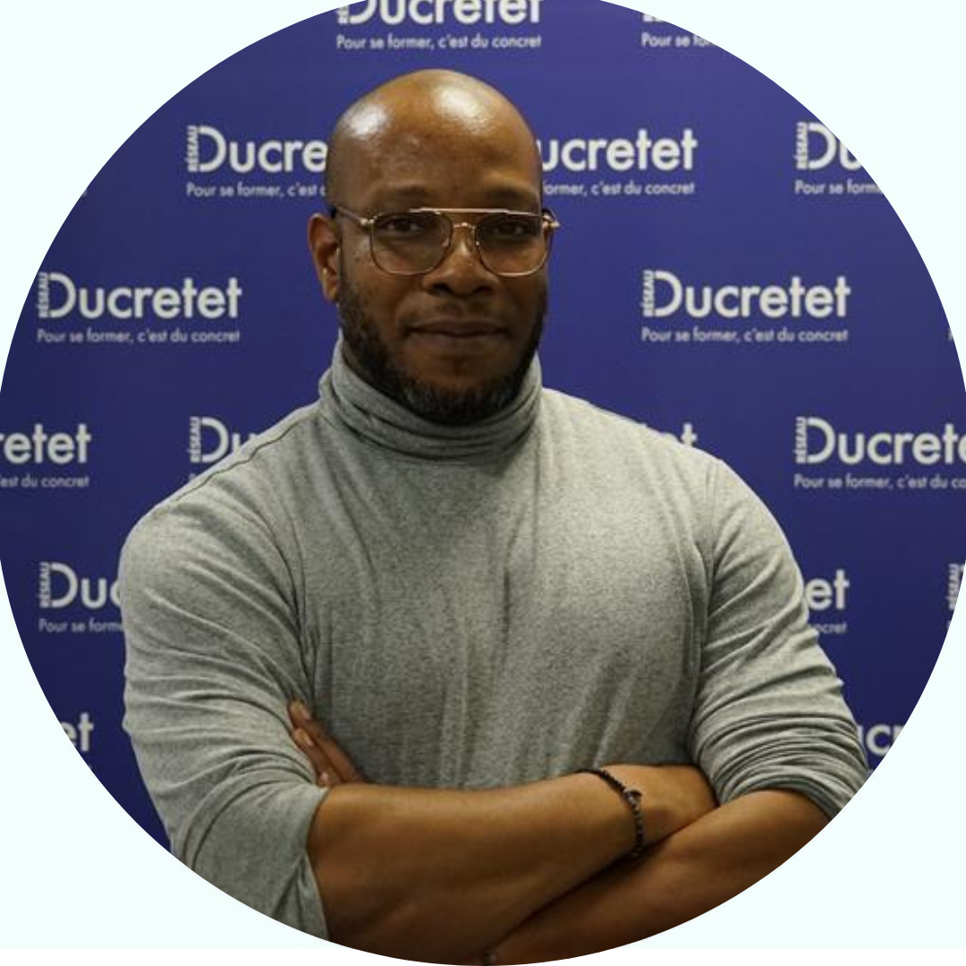 Un homme portant des lunettes et un col roulé, les bras croisés, devant un fond bleu « Ducretet ».