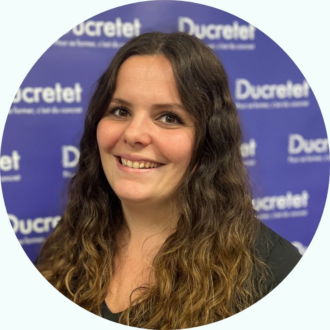 Une femme aux longs cheveux bruns sourit devant un fond bleu avec les logos « Ducretet ».