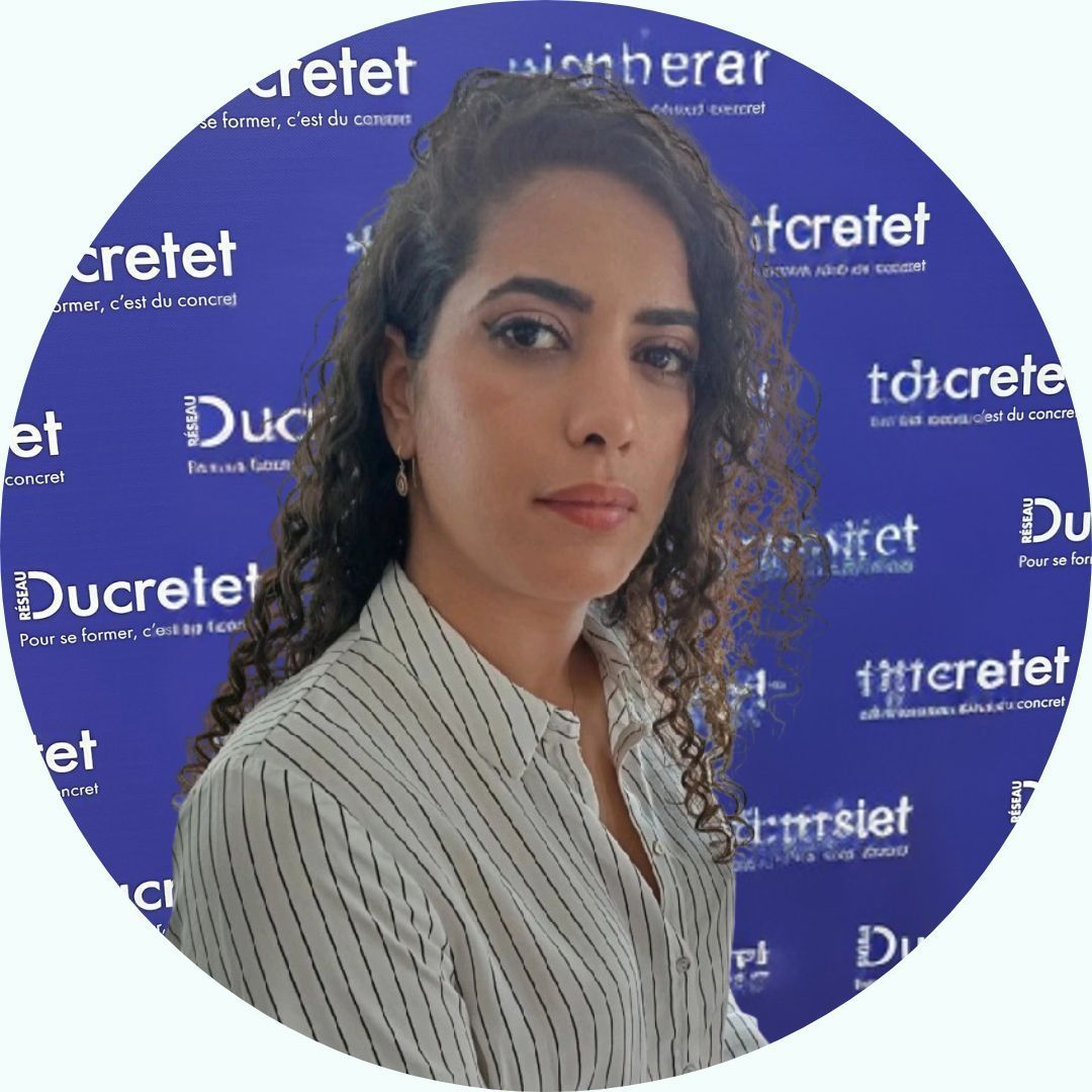 Femme aux cheveux bouclés, vêtue d'une chemise rayée, regardant la caméra, devant une fenêtre.